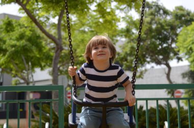 Küçük mutlu çocuk dışarıda salıncakta eğleniyor. Parkta salıncakta sallanan pozitif çocuk eğleniyor. Mutlu çocuk sallanmaktan zevk alır. Sevimli bir anaokulu çocuğu portresi.