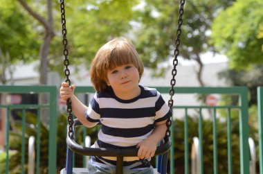 Küçük mutlu çocuk dışarıda salıncakta eğleniyor. Parkta salıncakta sallanan pozitif çocuk eğleniyor. Mutlu çocuk sallanmaktan zevk alır. Sevimli bir anaokulu çocuğu portresi.