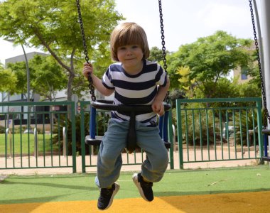 Happy little boy having fun on a swing outdoor. Positive boy having fun on a swing on the playground in public park. Happy child enjoy swinging. portrait of cute preschool laughing boy