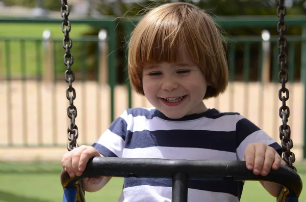 Küçük mutlu çocuk dışarıda salıncakta eğleniyor. Parkta salıncakta sallanan pozitif çocuk eğleniyor. Mutlu çocuk sallanmaktan zevk alır. Sevimli bir anaokulu çocuğu portresi.