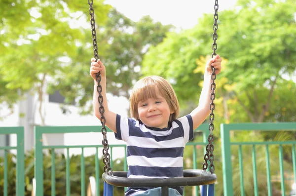 Küçük mutlu çocuk dışarıda salıncakta eğleniyor. Parkta salıncakta sallanan pozitif çocuk eğleniyor. Mutlu çocuk sallanmaktan zevk alır. Sevimli bir anaokulu çocuğu portresi.