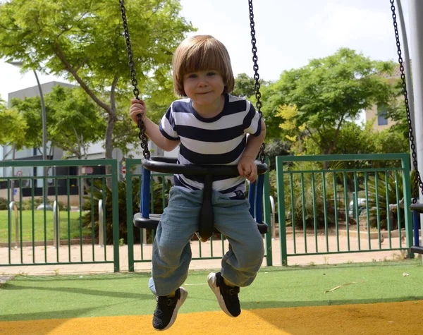 Küçük mutlu çocuk dışarıda salıncakta eğleniyor. Parkta salıncakta sallanan pozitif çocuk eğleniyor. Mutlu çocuk sallanmaktan zevk alır. Sevimli bir anaokulu çocuğu portresi.
