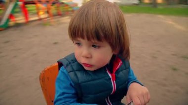 A little boy rides on a swing in the playground. Circular video.