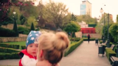 Oğlan 2 yaşında, büyükannesiyle parkta yürüyor. Parlak kırmızı ceket ve mavi şapka. Anne ve güneş. bahar