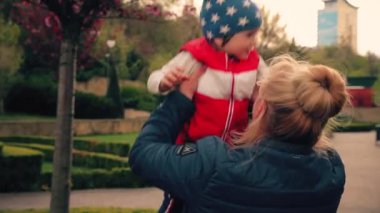 Boy 2 years old, walking with grandmother in the park. Bright red jacket and blue cap in the stars. Mom and sun. spring