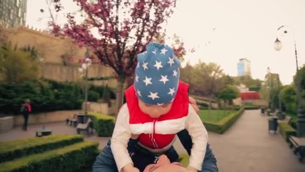 男孩2岁 和奶奶在公园里散步 明亮的红色夹克和蓝色的帽子在星空中 妈妈和太阳 — 图库视频影像