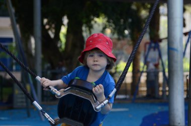 Avrupalı çocuğun salıncakta sallandığı günlerde oyun parkında oynayan mutlu küçük çocuk. Panama şapkalı çocuk.