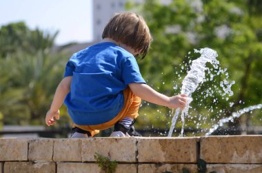 Çeşmede sevimli bir çocuk oynuyor. Yaz. Kavram: Sıcak hava. Çocuk suya su sıçrıyor..