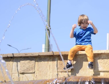 A cute boy is playing in the fountain. Summer. Concept: hot weather. The child splashes in the water.