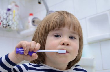 Küçük sarışın çocuk ev banyosunda dişlerini fırçalamayı öğreniyor. Çocuk nasıl sağlıklı kalacağını öğreniyor. Sağlık hizmeti konsepti. Sevimli çocuk gülümsüyor.