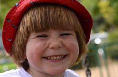 Küçük çocuk gülüyor. Yakın plan portre. Kırmızı panama şapkalı kızıl saçlı çocuk. Samimi gülümseme, süt dişleri