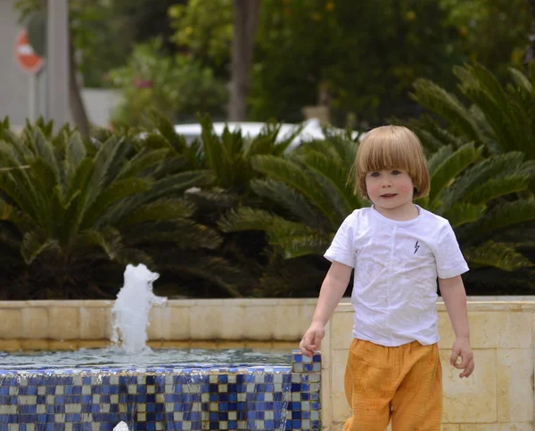 噴水で可愛い男の子が遊んでいる 黄色のパンツの子供は夏と晴れた日に喜びます 子供と一緒に歩く — ストック写真