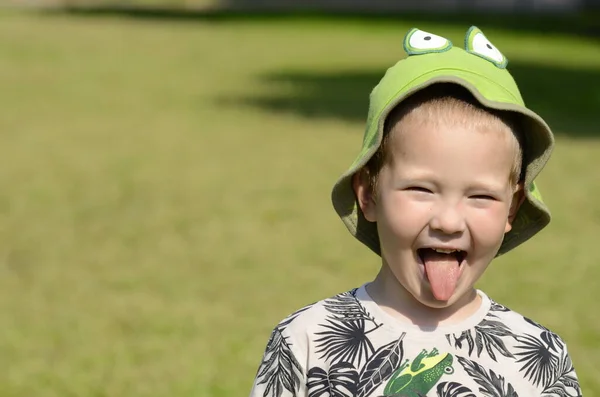 一个绿色背景的可爱男孩的阳光画像 那孩子笑了 露出舌头 有青蛙眼睛的巴拿马帽 — 图库照片