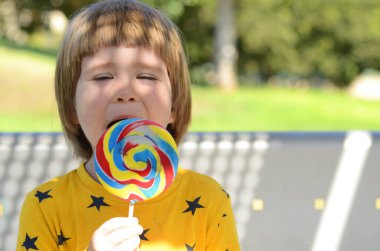 Yaz havası. Tatlı bir çocuk büyük bir lolipop yiyor. Parlak güneş. Konsept: Aile tatili, anaokulu, yaz aktiviteleri, eğlence