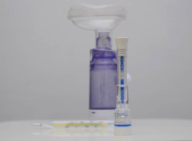 IgM / IgG antikorlarını ve dokunulmazlığı tespit etmek için 15 dakika içinde Covid-19 test kiti. İki şerit, pozitif. Arka planda ilaçlar, şuruplar, bir termometre, bir astım spreyi var.