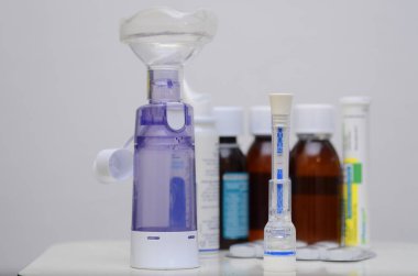 IgM / IgG antikorlarını ve dokunulmazlığı tespit etmek için 15 dakika içinde Covid-19 test kiti. İki şerit, pozitif. Arka planda ilaçlar, şuruplar, bir termometre, bir astım spreyi var.