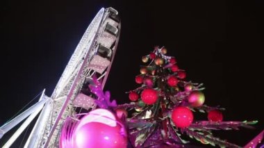 Şenlikli çelenkler içinde dönme dolap. Işıklar ve toplarla süslenmiş Noel ağacı. Noel pazarı, akşam, günün karanlık zamanları. Kavram: Noel, kış, Aralık, tatiller