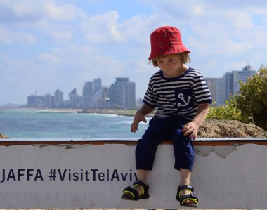 Tel Aviv 'i ziyaret et. Yelek giymiş küçük bir çocuk ve deniz ve şehir sınırına karşı komik bir panama şapkası. Selfie için bir yer..