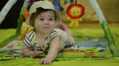 6 aylık Avrupalı bebek, orman oyun hasırında safari şapkası takıyor. Sevimli bebek gülüyor, paspasla oynuyor. Çocuk kameraya gülümsüyor..