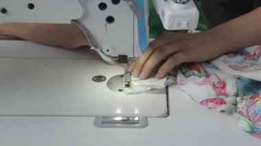 Dikiş fabrikası. İşteki kadın elbise fabrikasında dikiş dikiyor. Video yakın çekim. İğne ve dikiş makinesi, fabrikada kadın elleri dikiş diker. El emeği.