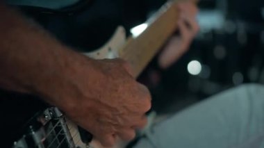 Yaşlı bir adam elektro gitar çalar. Telleri koparan bir elin yakın çekimi. Rock müzisyeni provada ya da canlı performansta