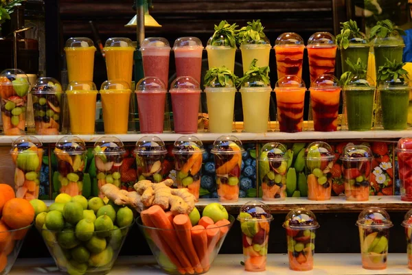 Briht stools in front of colorful fruit juice stall in Carmel Market Tel Aviv. Showcase with cups of smoothies and fruit cocktails. Juicy fresh fruit slices in plastic cups