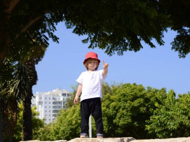 Funny kid on the background of a residential area, new buildings. Boy in the park near the house. Boy in full growth Concept: family property. Space for text.