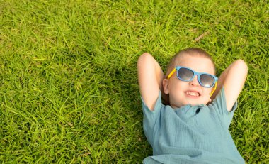 Boy schoolboy lies on a green meadow on the grass. A child with sunglasses is resting, enjoying the summer. Dreams about travel, sea, adventure, amusement park, birthday