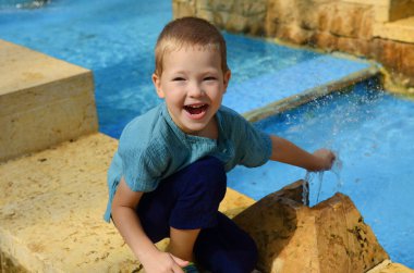 A little boy is playing in the fountain. Summer games, jet of water on a hot day. The child laughs. Water activities on the streets of the city