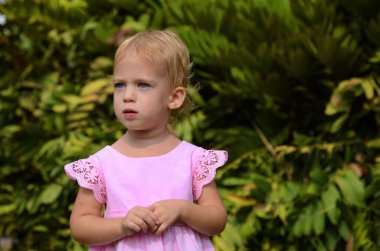 Positive baby, two years old. Portrait of a little girl on a walk. Cute daughter in a pink dress