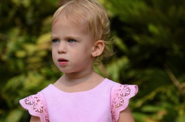 Positive baby, two years old. Portrait of a little girl on a walk. Cute daughter in a pink dress