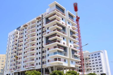 Sunny day, construction site, construction crane. New building in Israel. Concept: real estate agency, apartment on credit, real estate investment. Modern white residential building