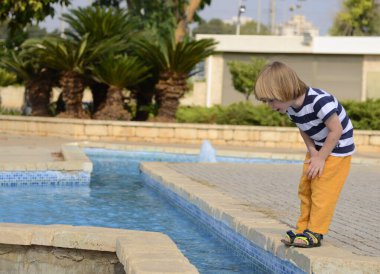 A little boy is playing by the fountain. Concept: hot weather, summer holidays, kindergarten, water activities, summer in the city