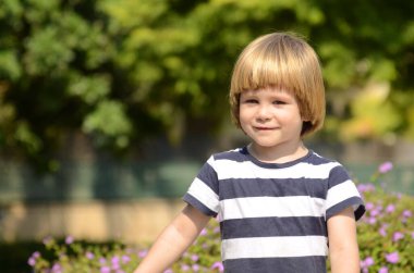 Cute boy, smilling. Close-up portrait against the background of violet flowers. Little boy with beautiful hair
