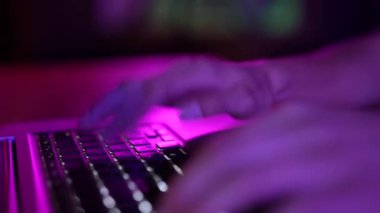Neon light, female hands on the keyboard of a computer, laptop. Close-up Concept: hacker, IT, job, junior, tester, programmer, typist, freelancer.