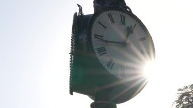 Antique street clock. Sunbeams, early morning, dawn. Close-up, forged watch, large dial.