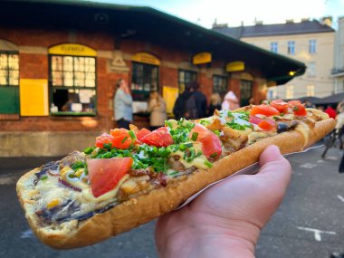 Lezzetli uzun cila Zapiekanka. Geleneksel Polonya fast food, sokak yemekleri. Peynirli, sosisli, domatesli sıcak sandviç. İkonik kraliyet güveci, Kazimierz 'de sarı tabela. Krakow Polonya Ekim 2022