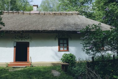 Ukrayna 'nın sazdan çatılı eski evi, pencerenin önünde ahşap bir bank ve yatay olarak mor çiçekler.