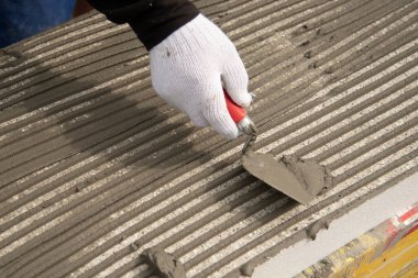 Ev yalıtımı için beyaz poliüretan köpük tabakasına yapıştırıcı süren beyaz eldivenli işçi elinin yakın çekimi..