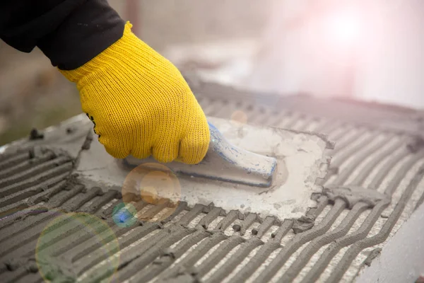 Close-up of worker hand, in yeiiow gloves with trowel applying glue on white rigid polyurethane foam sheet for house insulation.