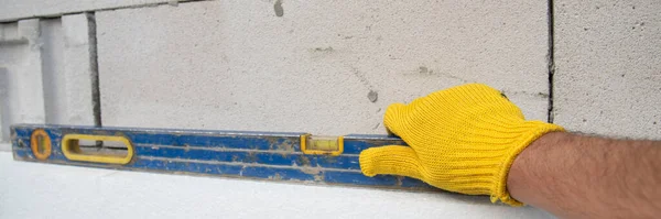 Construction worker insulating house wall with styrofoam insulatuion sheet, using of the construction spirit level.