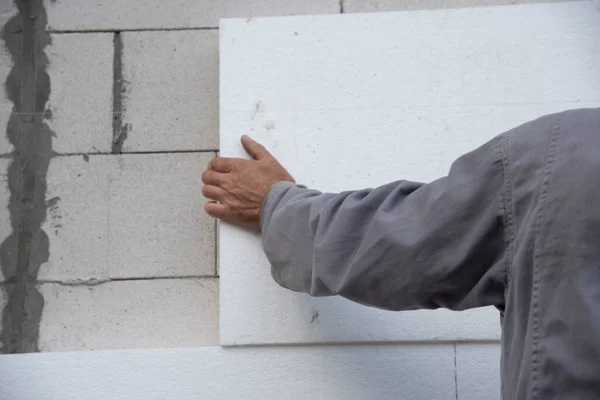 Construction worker installing styrofoam insulation sheets on house facade wall for thermal protection. Thermal insulation.