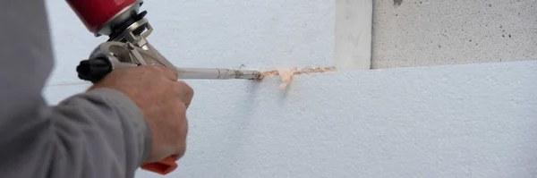 Construction worker installing styrofoam insulation sheets and filling space between with expanding foam on house facade wall for thermal protection. Thermal insulation.