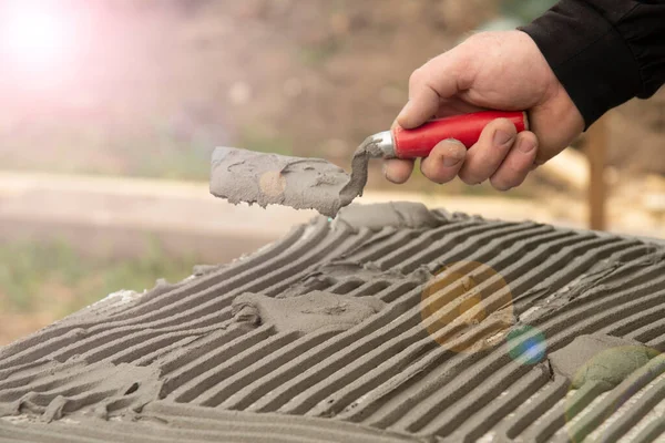 Close-up of worker hand, with trowel applying glue on white rigid polyurethane foam sheet for house insulation.