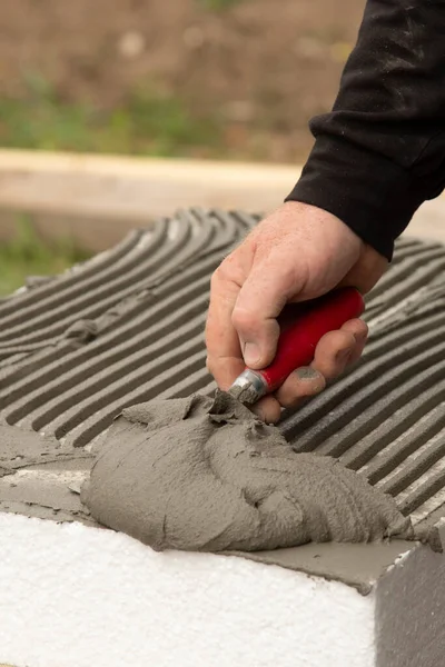 Close-up of worker hand, with trowel applying glue on white rigid polyurethane foam sheet for house insulation.