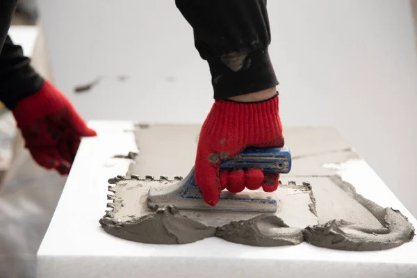 Close-up of worker hand, in red gloves with trowel applying glue on white rigid polyurethane foam sheet for house insulation.