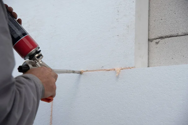 Construction worker installing styrofoam insulation sheets and filling space between with expanding foam on house facade wall for thermal protection. Thermal insulation.