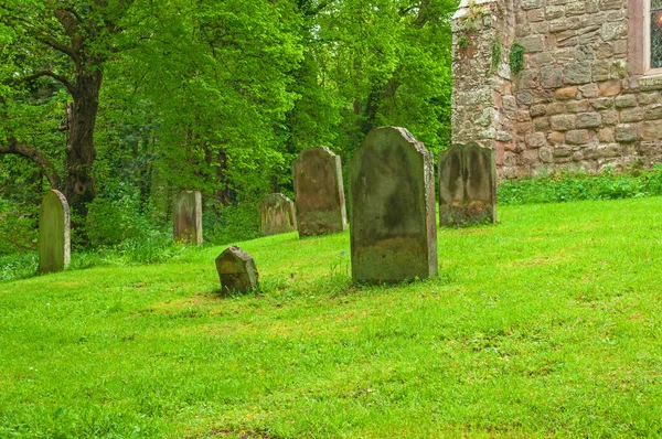 Rural graveyard, cemetery, ancient peaceful resting place set in green grass with trees, old stone hand crafted headstones worn and nameless from age