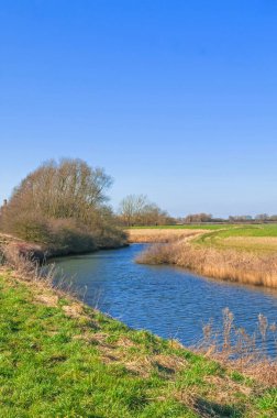 Steep banked river in winter, barren landscape, bare trees