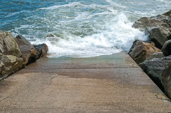 Stone slipway with blue ocean, sea breaking waves and rocks, danger, drowning, steep, 